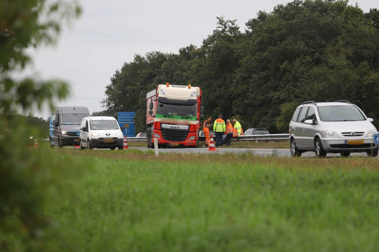 Kilometers file door vrachtwagen met klapband bij Opeinde