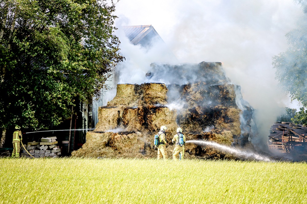 Grote stapel met hooibalen in brand naast loods