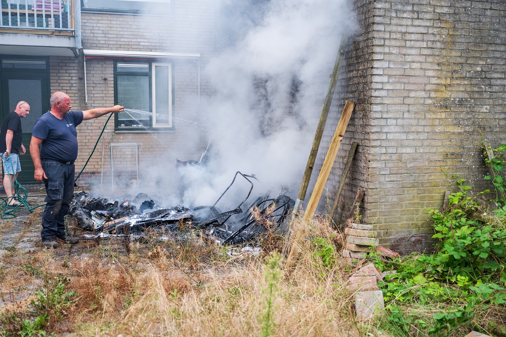 Omstanders blussen buitenbrand met tuinslang en brandblussers