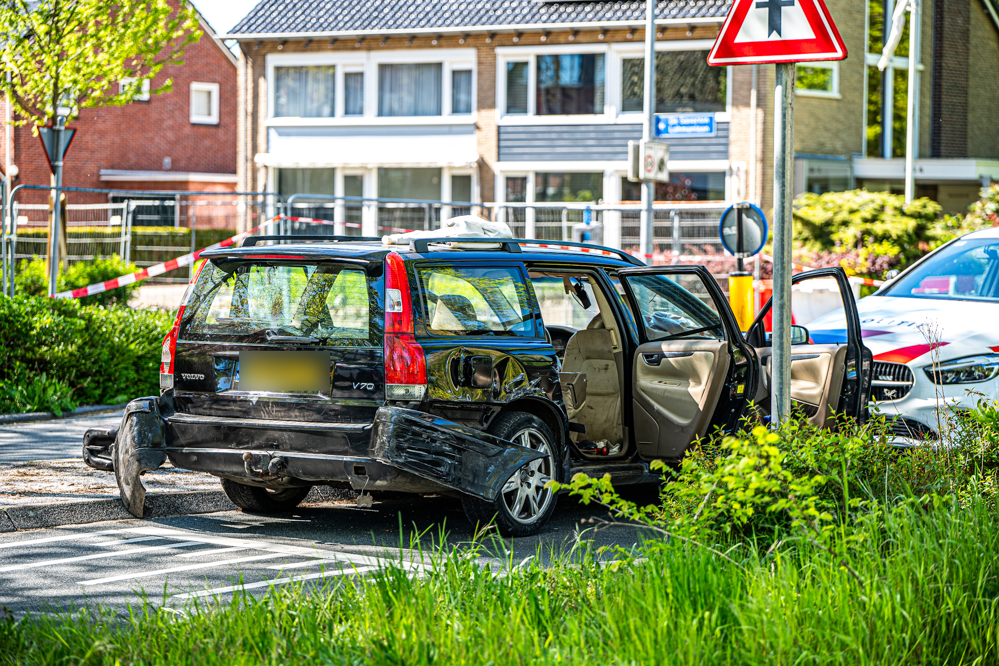Damaged black Volvo SUV with open rear door, taped-off street in a suburban neighborhood.