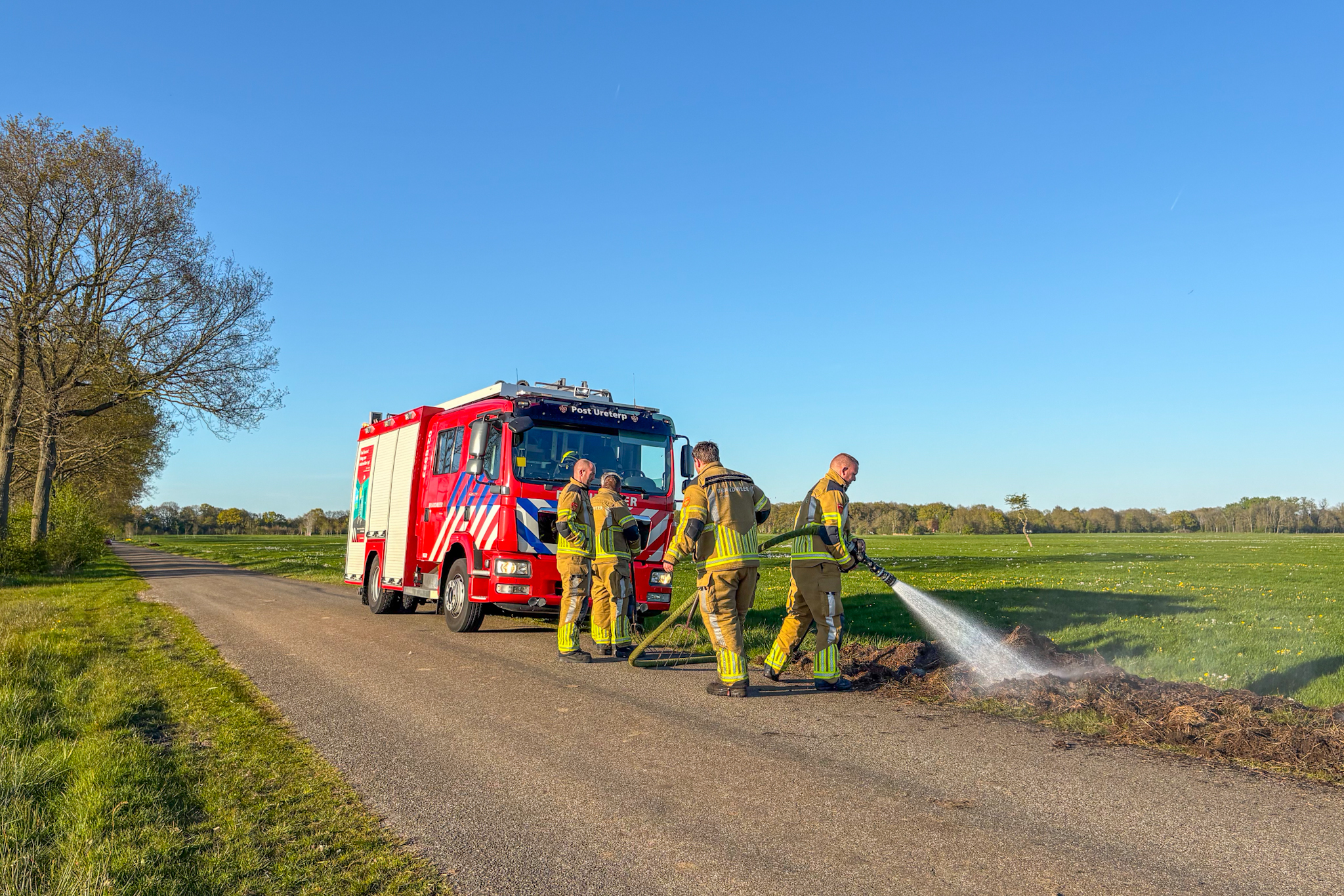 Brandweer blust brandende hopen gras en slootmateriaal