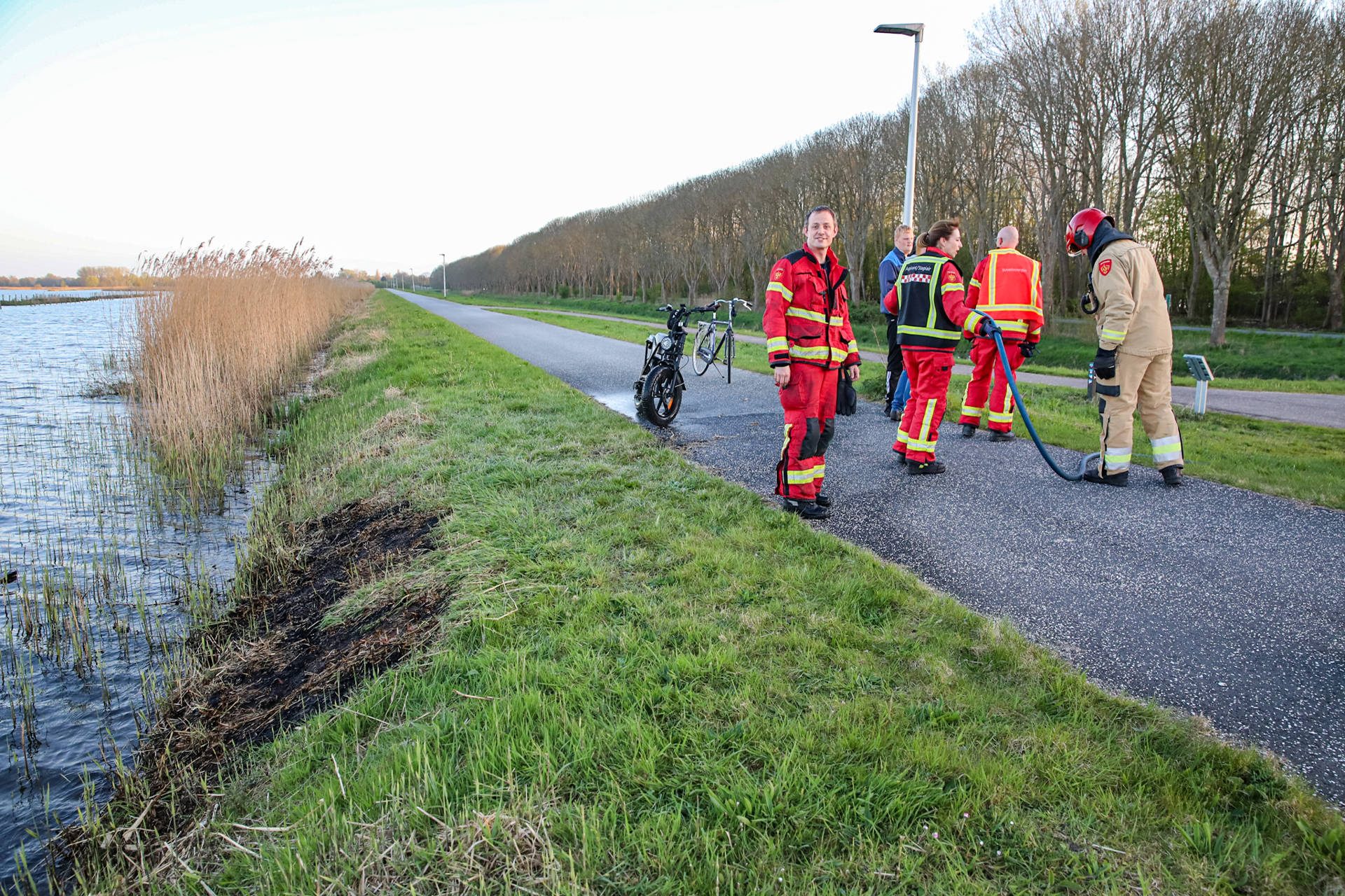 Brandweer blust rietbrand langs meer