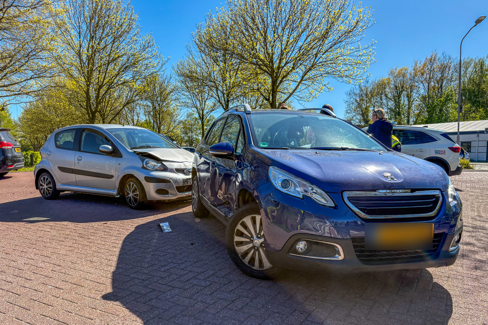 Blue Peugeot SUV in the foreground after a collision with a silver car in a parking lot on a sunny day.