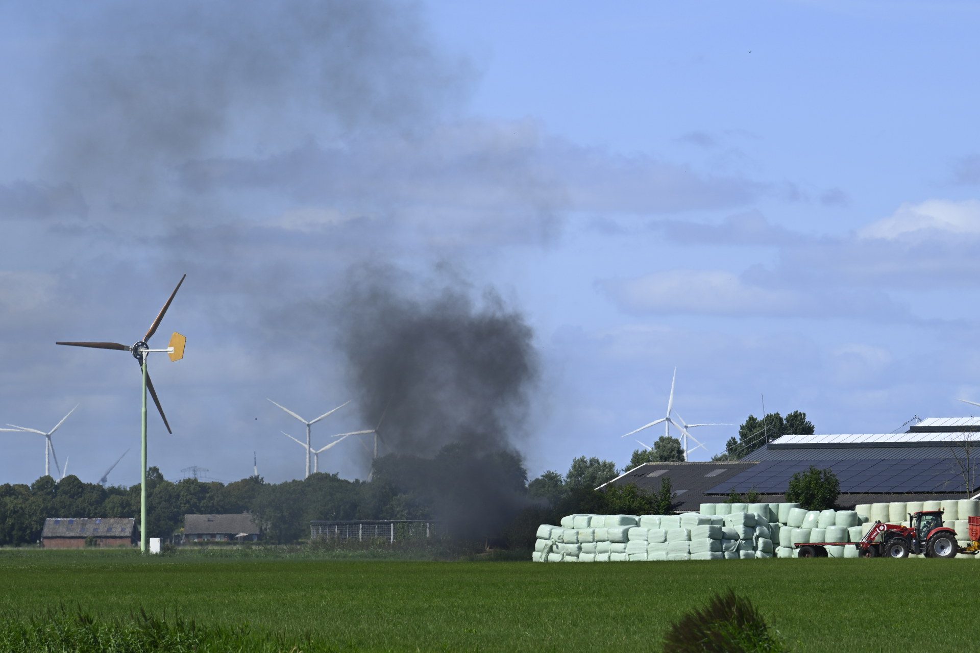 Grote zwarte rookwolk stijgt op achter boerenschuur bij afvalvuur